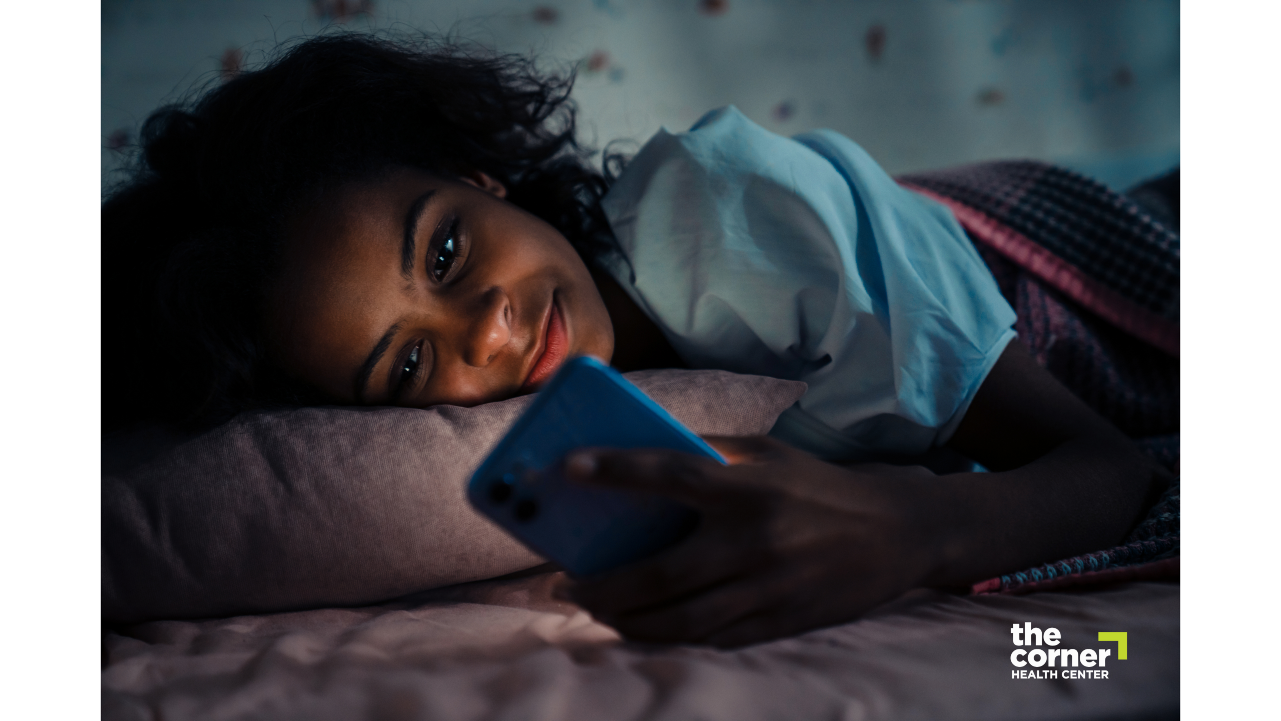 Teen girl laying in bed in the dark and staring at her phone.